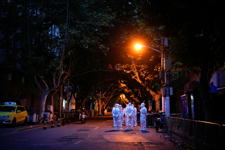 A half-dozen people wearing protective gear stand in a street under a street lamp.