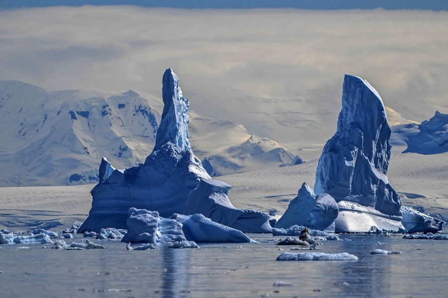 Tall icebergs float in a strait in front of snow-covered mountains.