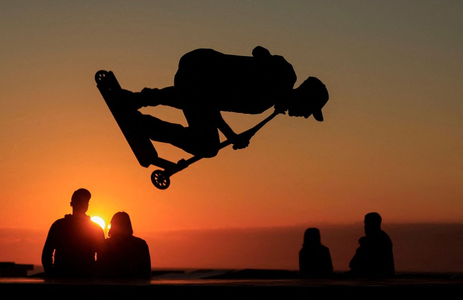 A person in silhouette jumps while riding a scooter at sunset.