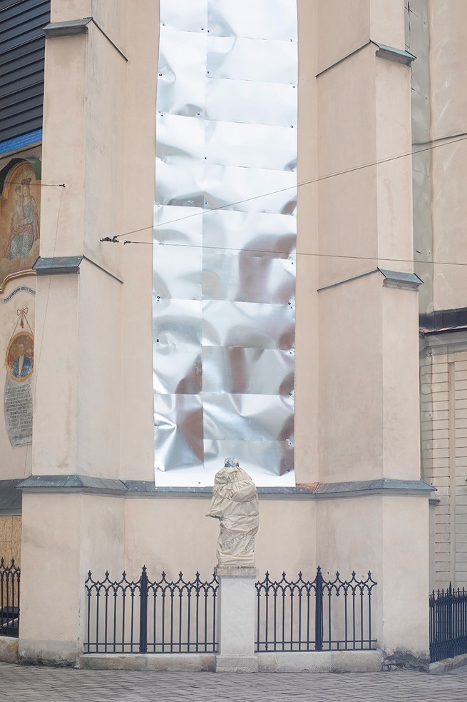 photo of a building's windows covered with metal behind an outdoor statue shrouded in protective cover