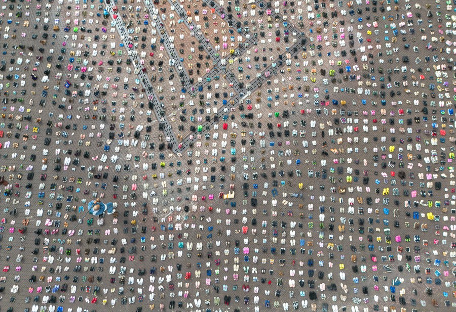 An overhead view of thousands of pairs of children's shoes, arranged in rows in a public square.
