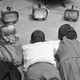Old black-and-white photograph of four kids lying on a carpet, watching four small televisions