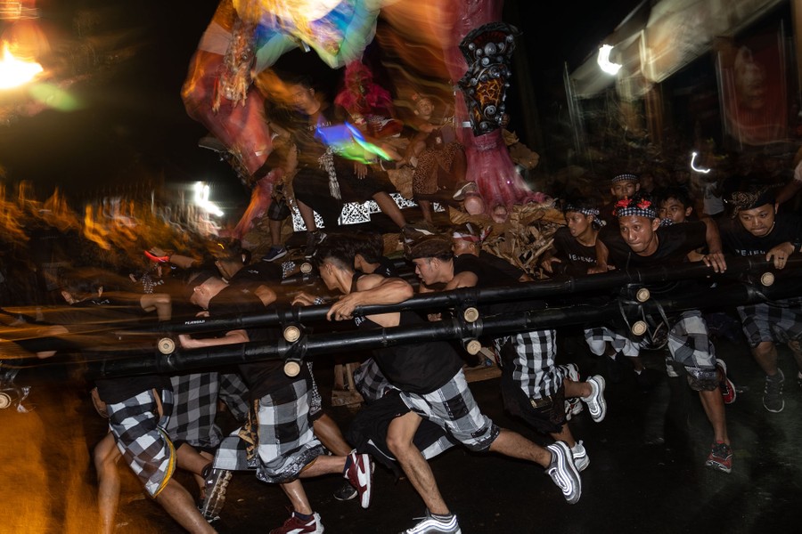 A group of people run while carrying a sculpture on a parade route.