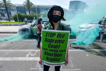 Picture of a masked girl with a sign that reads "STOP the Supreme Court from taking away Abortion Rights!"