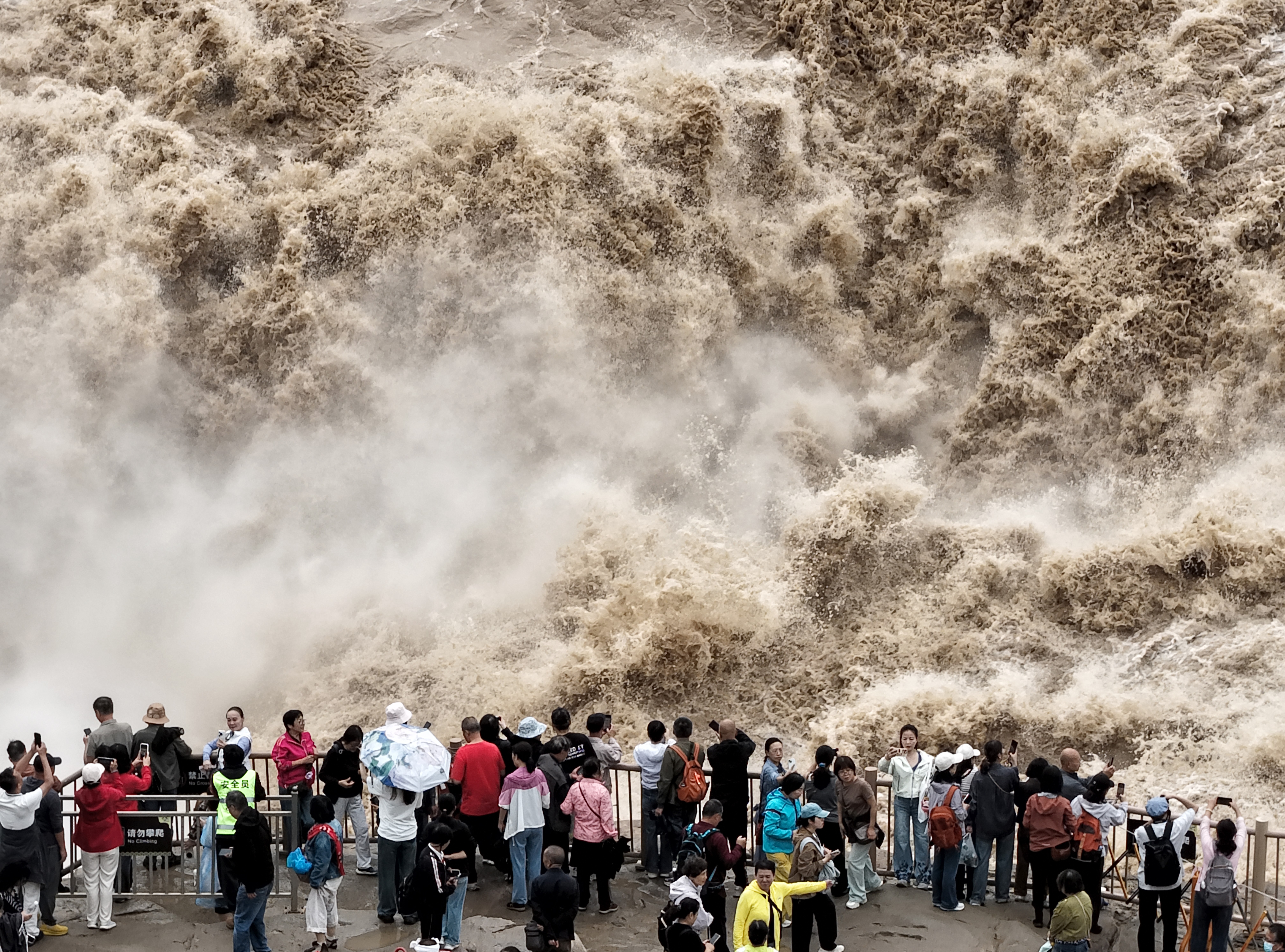 A crowd watches from an observation area as turbulent water, splashes, and rushes past.