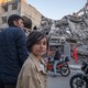 People including two young girls standing in front of rubble in a residential area in Tehran