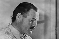 A black-and-white photo of Ernest Hemingway working at a typewriter