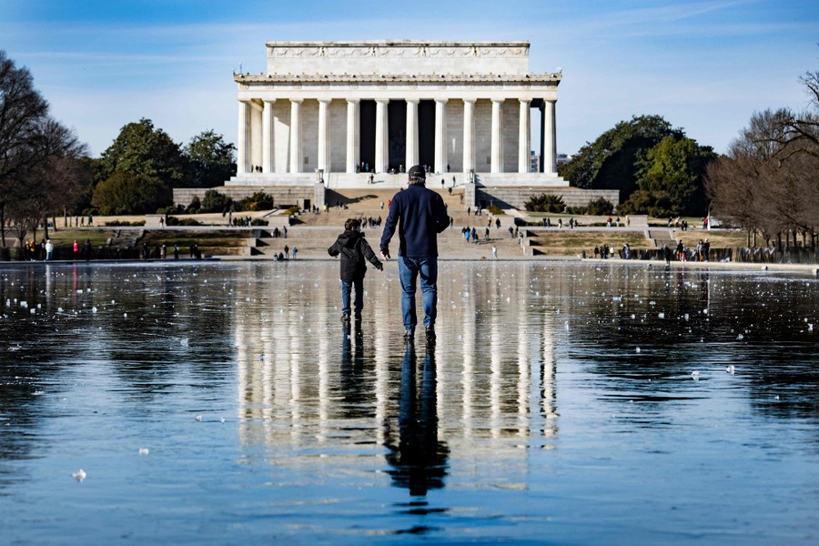 A man and a boy walk across the frozen Reflecting Pool toward the Lincoln Memorial.