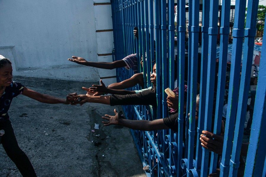 People reach their arms through the bars of a fence.