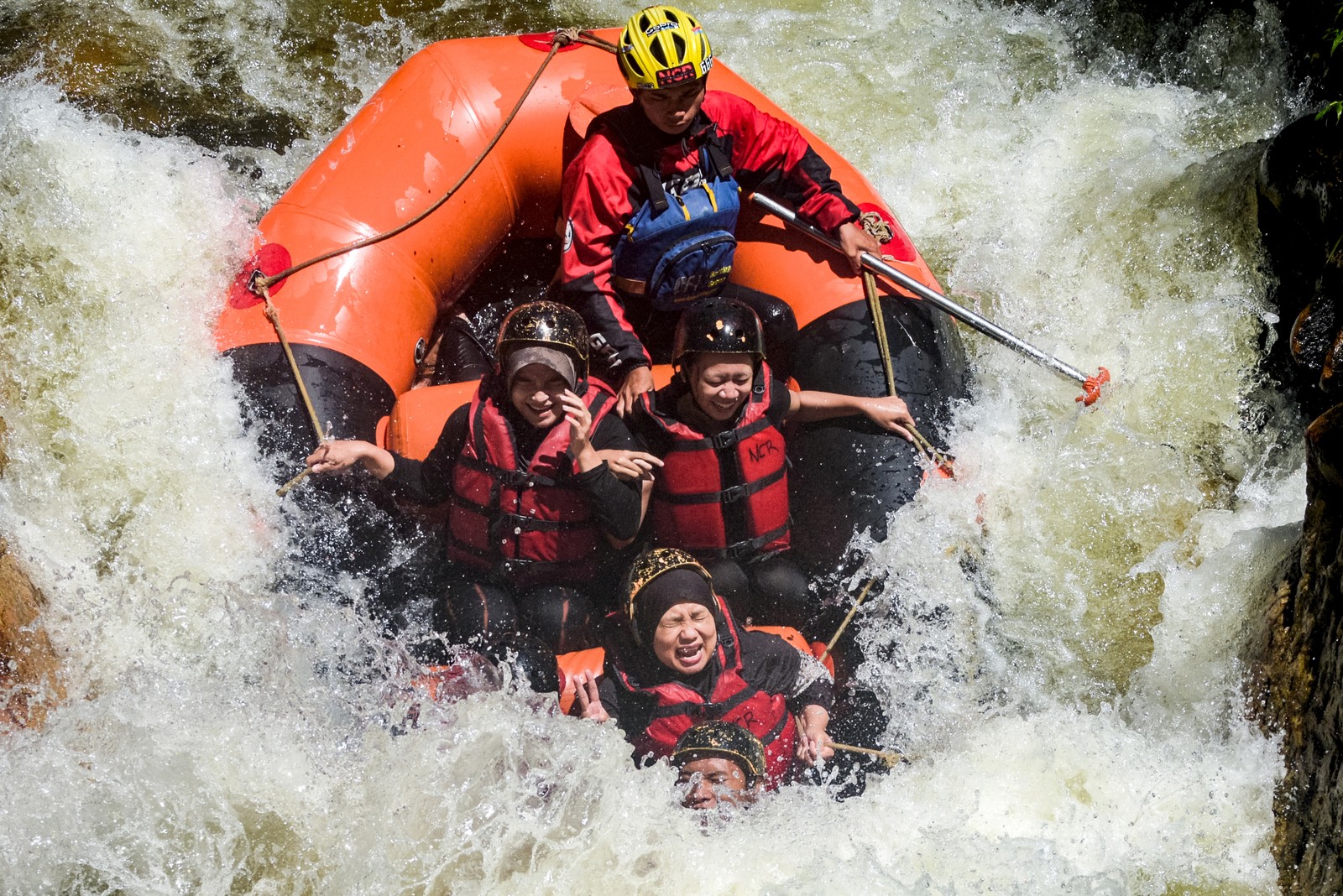 Five or six people wearing life jackets ride a rafts over a steep stretch of rapids.