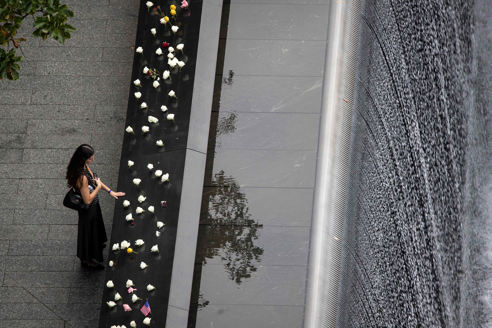 An elevated view of a person standing along the September 11 memorial, above a cascade of water.