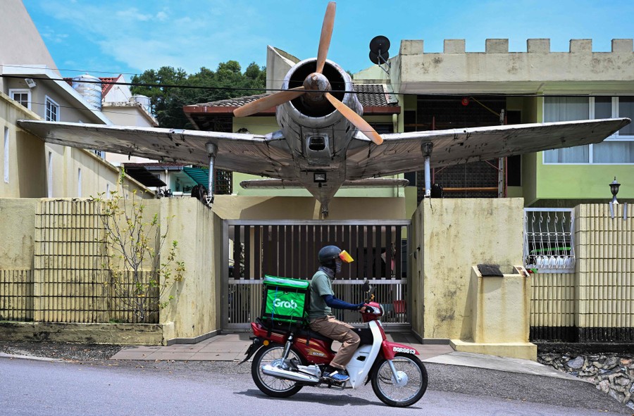 A delivery person rides a motorbike in front of a house decorated with a full-size aircraft.
