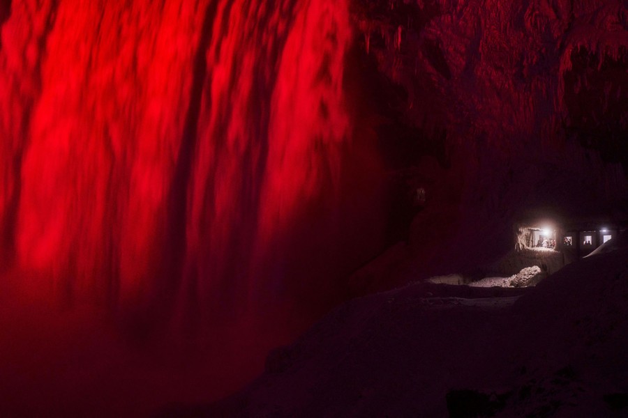 A section of a large waterfall is lit red at night.