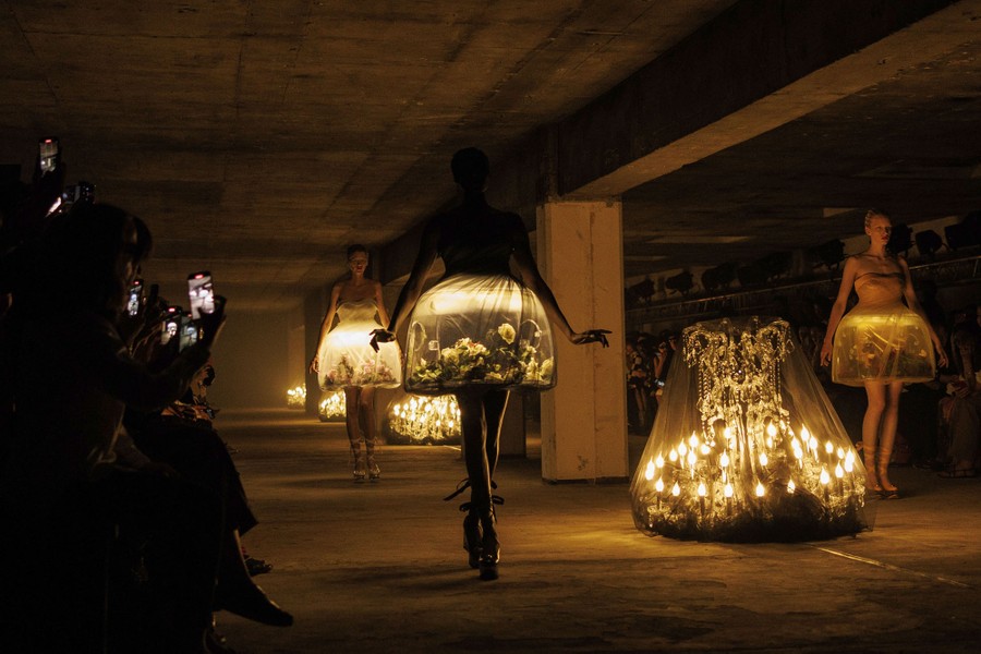 Models walk on a dimly-lit runway, wearing garments that are lit from within.