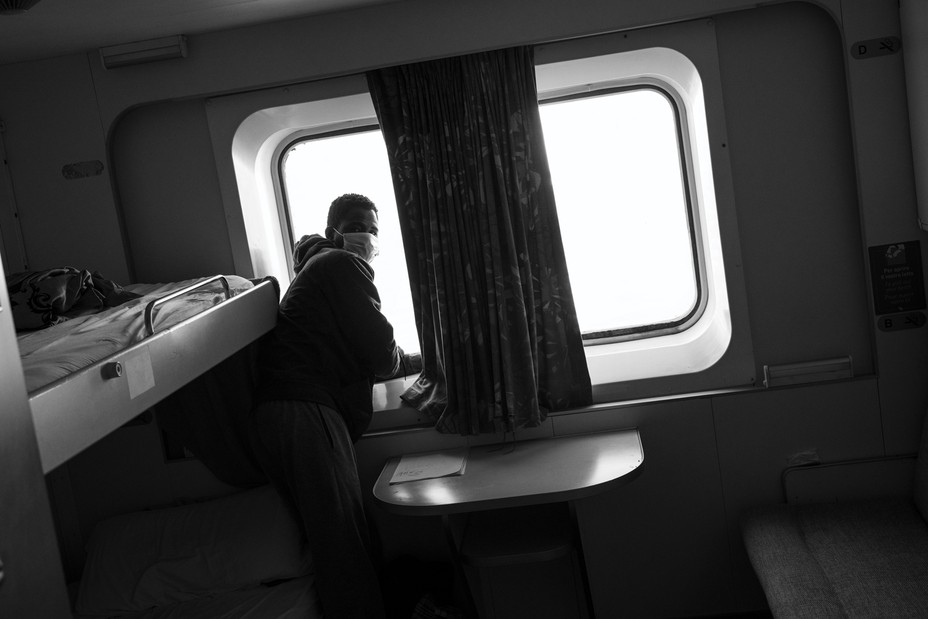 A migrant standing by a window in the ship's cabin