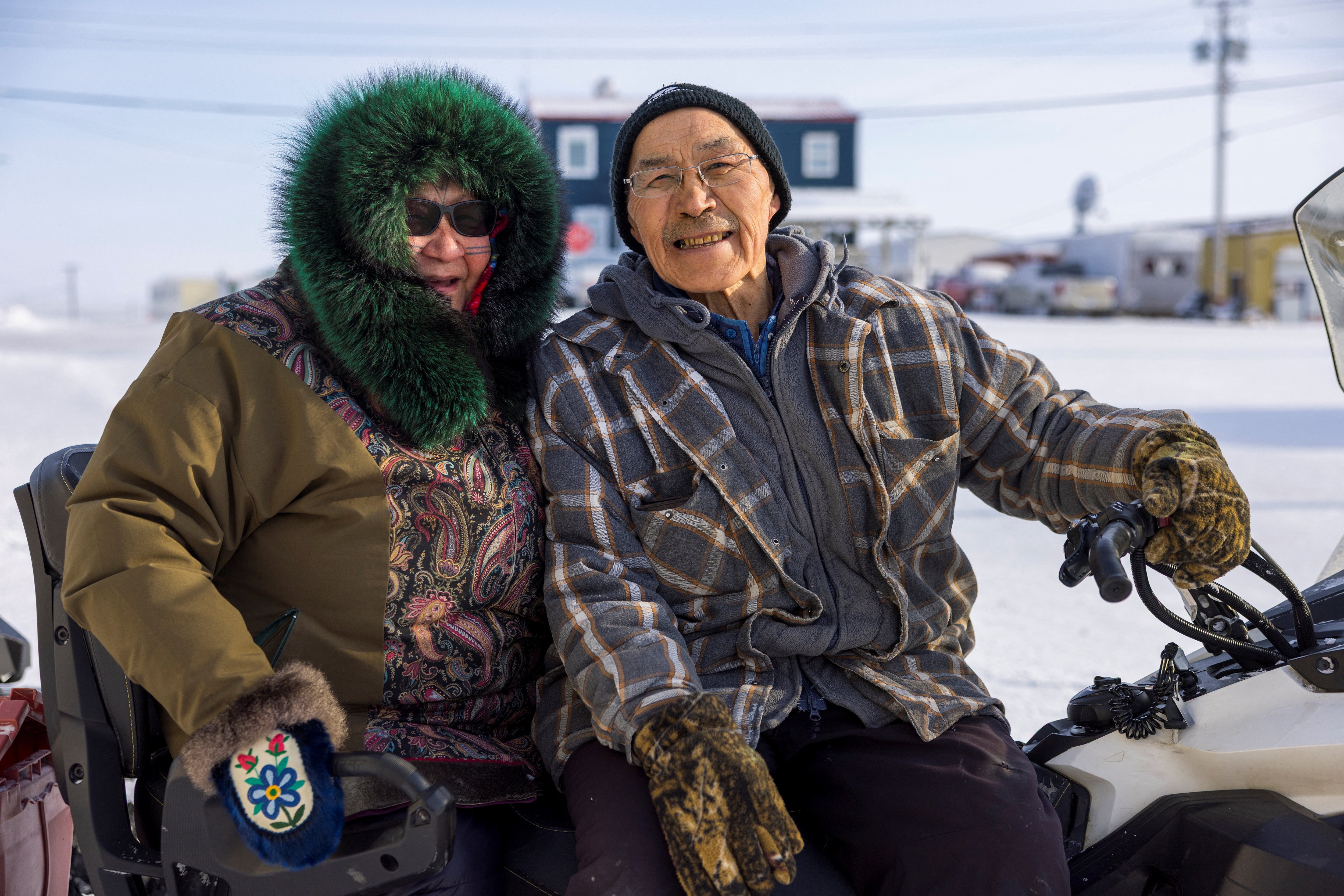 A couple dressed in warm clothing smile and pose for a photo while sitting on a snowmobile.