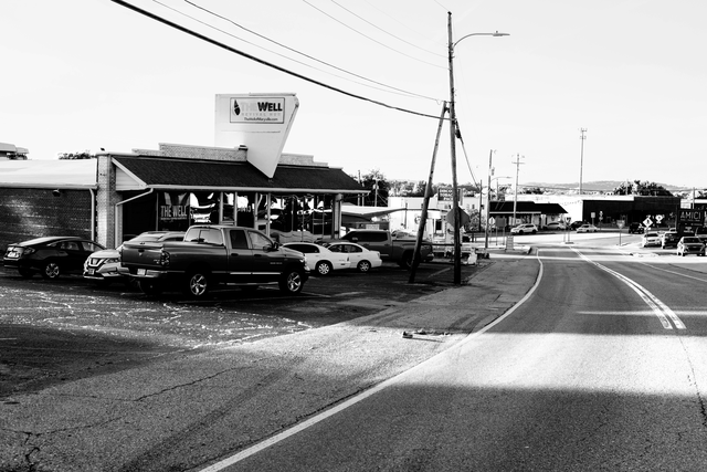 black-and-white photo of former-grocery-store-turned-church with crowded parking lot at side of two-lane road in small town