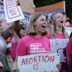 A view of several people in a larger crowd, marching and carrying pro-abortion-rights signs.