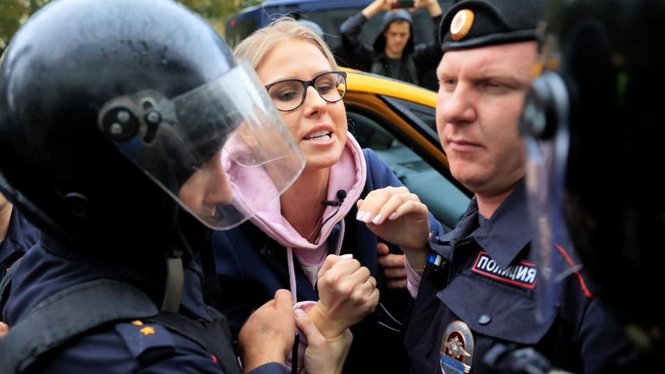 Law enforcement officers grab Lyubov Sobol's hands as she emerges from a taxi.