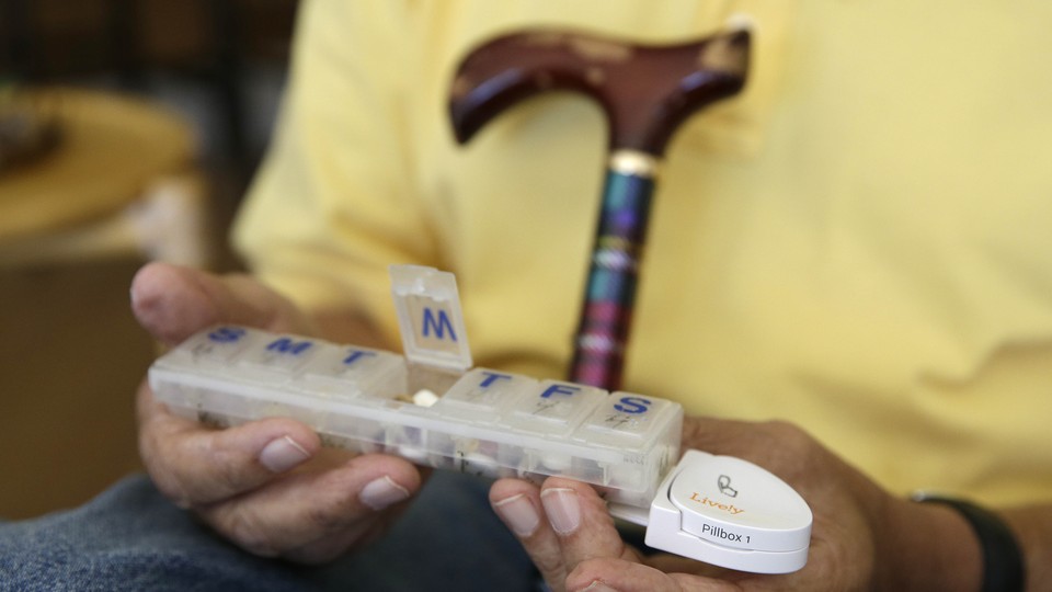 An older person holds a pillbox with sections for days of the week.