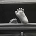A baby's feet stick out of a stroller in a black-and-white photo.