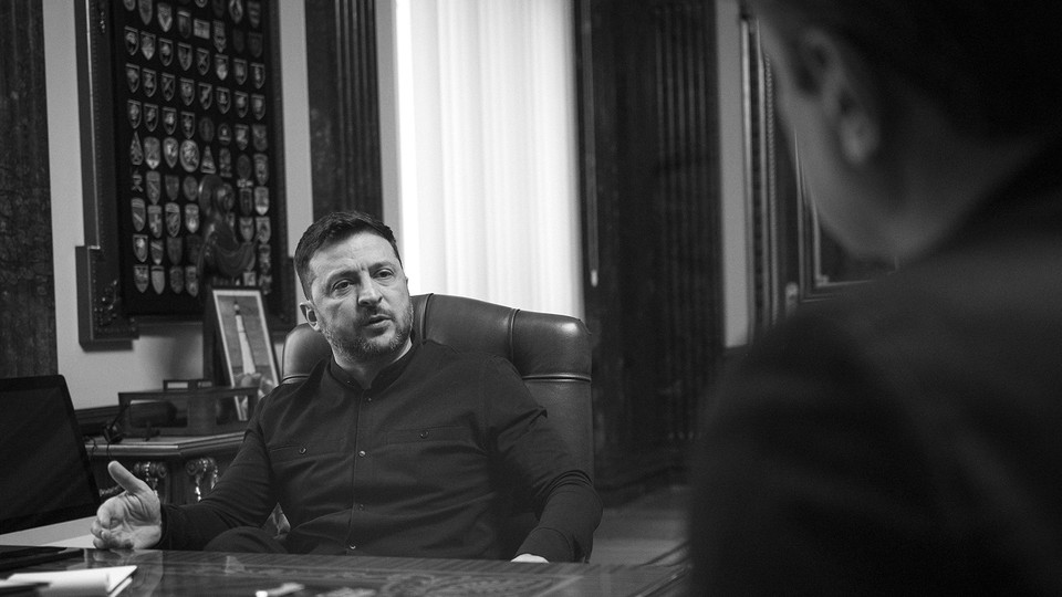 A black-and-white photograph of Volodymyr Zelensky seated and gesturing