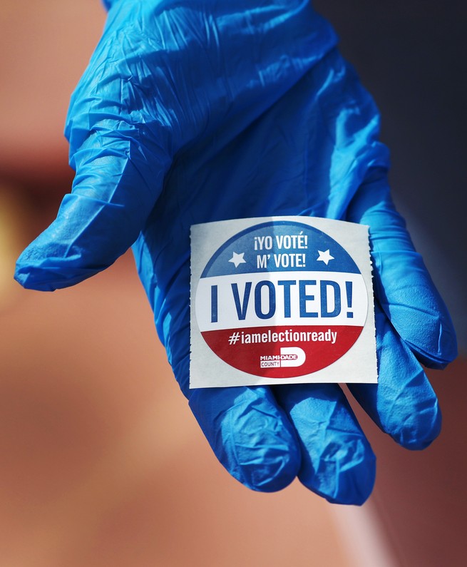 A gloved hand holding an "I Voted" sticker.