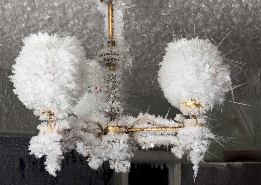 Ice crystals completely cover a small chandelier and the ceiling it hangs from.