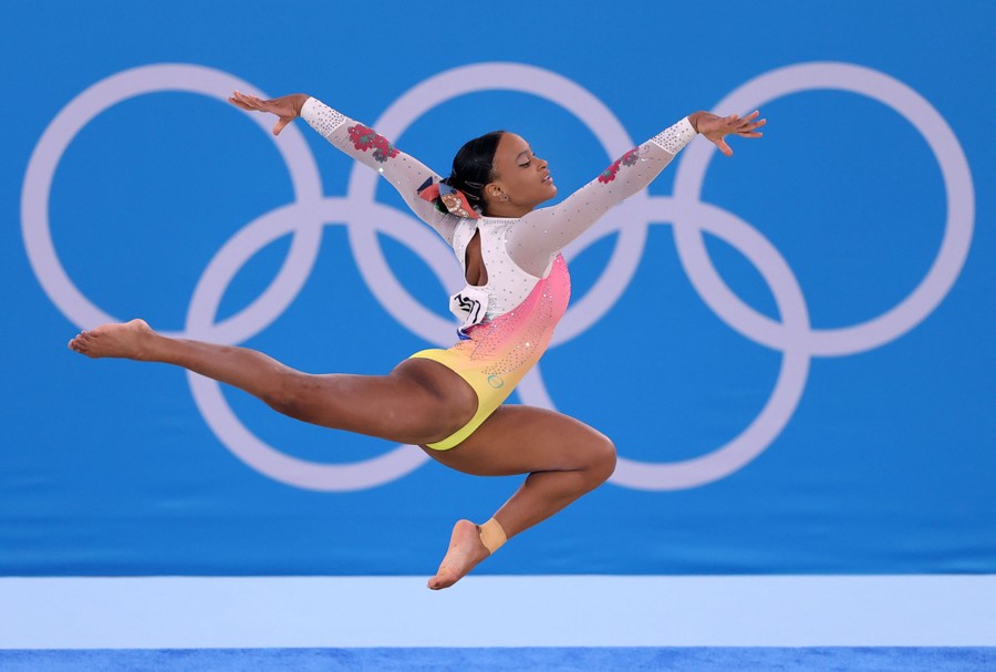 A gymnast leaps in front of a wall with an image of the Olympic Rings.