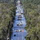 About a dozen utility trucks sit in the middle of a flooded road, seen from above.