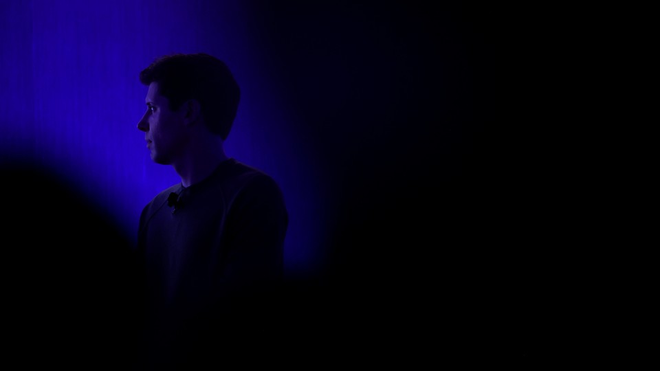Photograph of Sam Altman in a dark room, his shoulders and face illuminated by a blue light