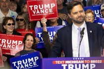 A news photo of J. D. Vance at the podium with Trump-Vance supporters waving placards.