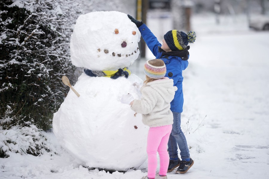 Two children build a snowman taller than they are.