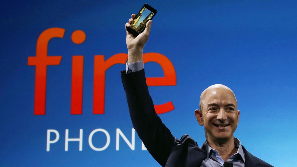 Amazon's Jeff Bezos smiles and holds a phone in the air.