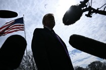 An image of Trump's silhouette from below surrounded by microphones, with an American flag flying in the background.