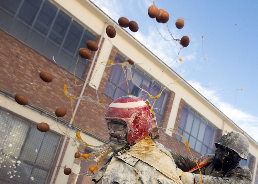 A person wearing a helmet is pummeled by thrown eggs.