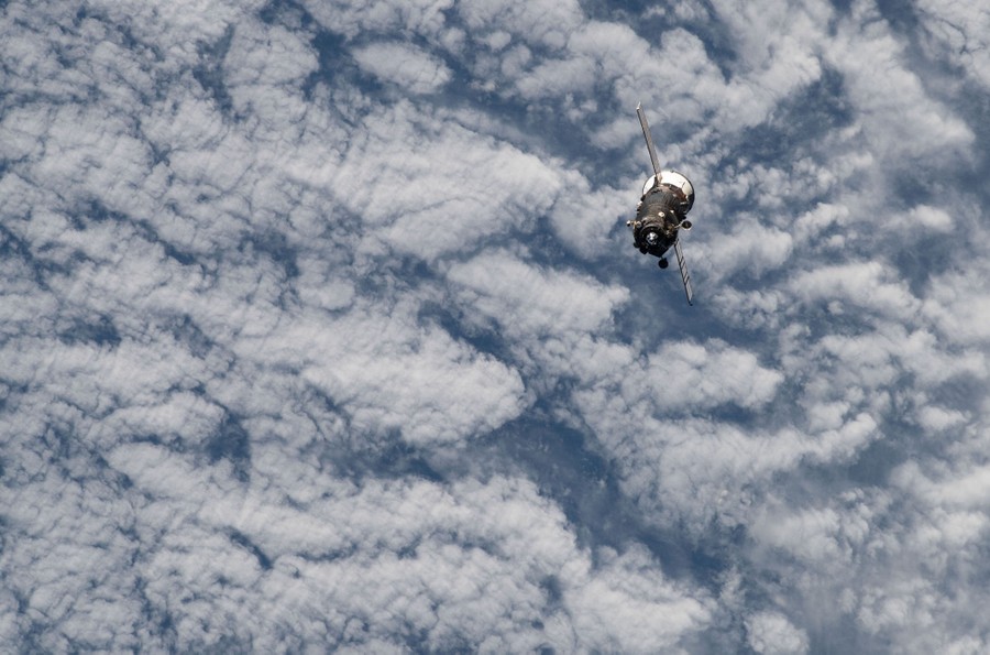 A spacecraft floats above cloud cover, seen from above.