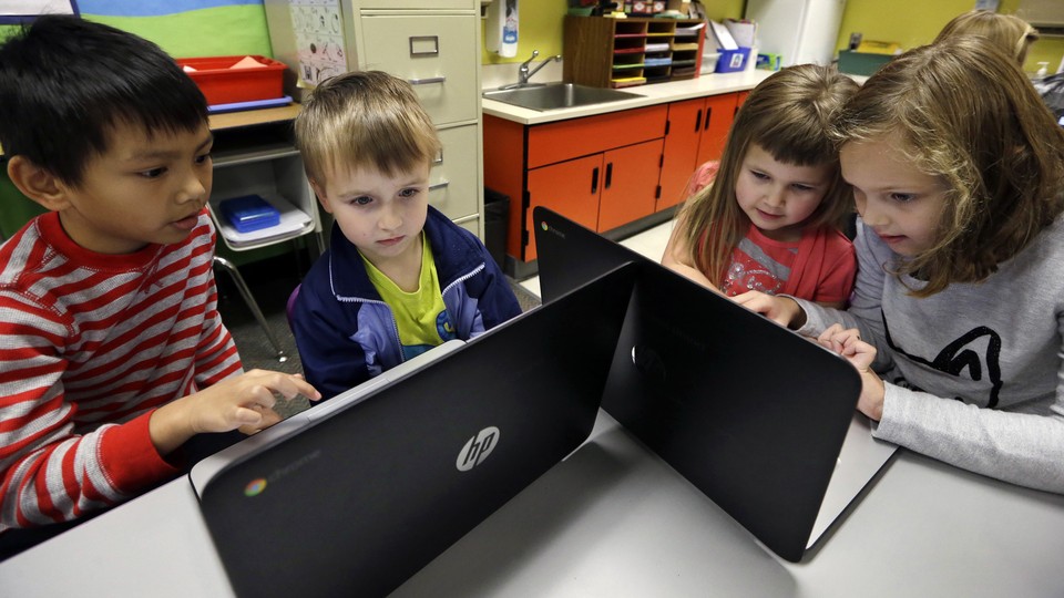 Two boys and two girls huddle around two laptops.