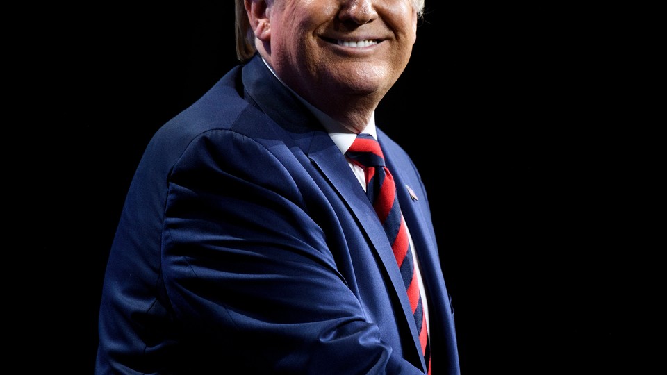 President Donald Trump looking to his right and smiling, wearing a navy suit with a red-and-blue-striped tie