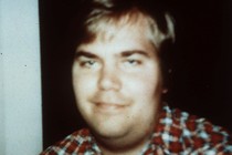 A photo of John Hinckley taken in 1999 shows him smiling and wearing a plaid shirt.