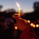 Color photograph of a single candle being held aloft at a vigil.