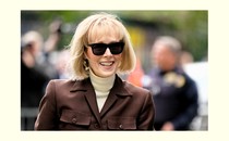 Photo of E. Jean Carroll wearing sunglasses, a white turtleneck, and a brown jacket
