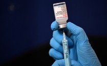 An image of a pair of gloved hands inserting a syringe into a vaccine vial