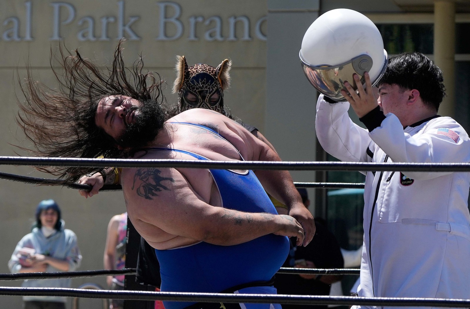 A pro wrestler flings his head back after being struck by another wrestler holding an astronaut helmet.
