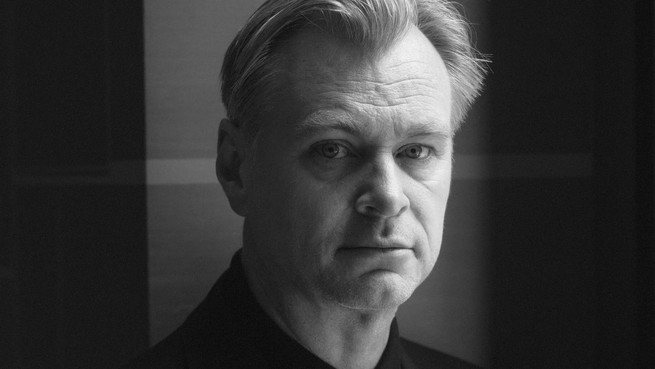 A black-and-white photo of Christopher Nolan looking into the camera