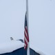A white raven sitting on a snow-covered roof next to an American flag in Anchorage, Alaska