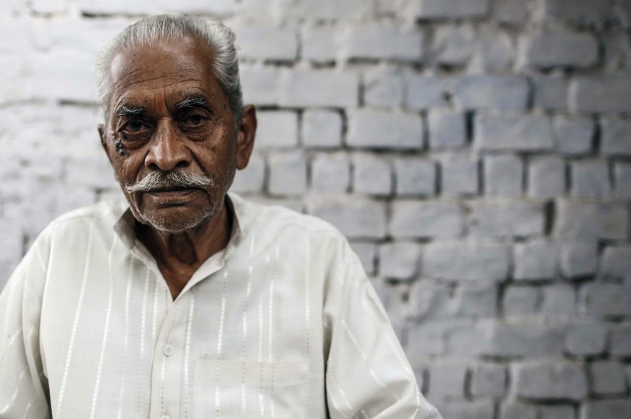 The same man from the previous photograph, looking older, sits alone.