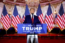 Trump standing behind a lectern with a sign that says "Trump 2024"