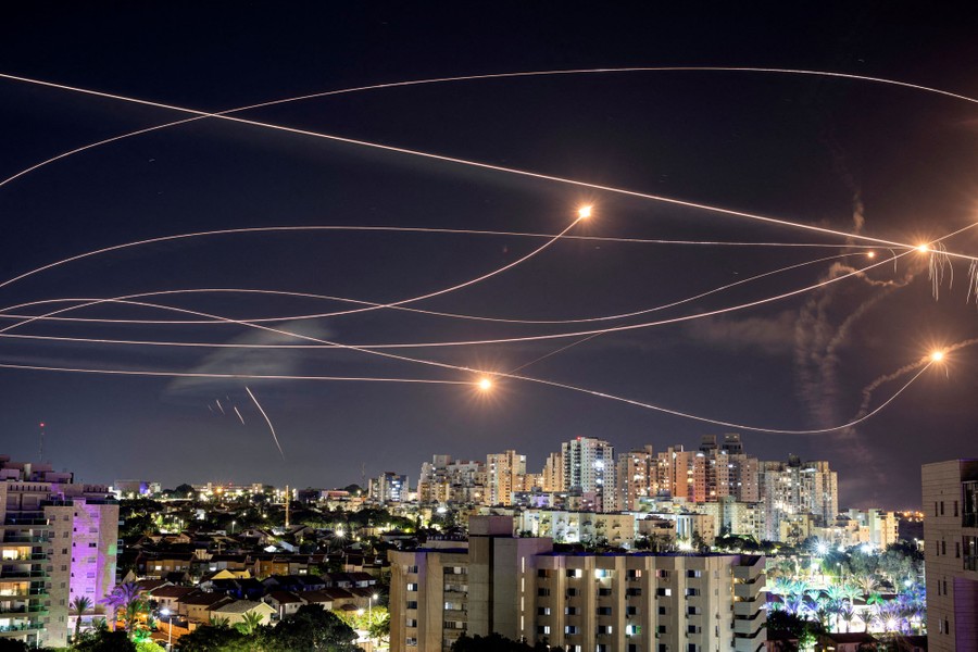 Streaks and lights from several missiles in the night sky above buildings