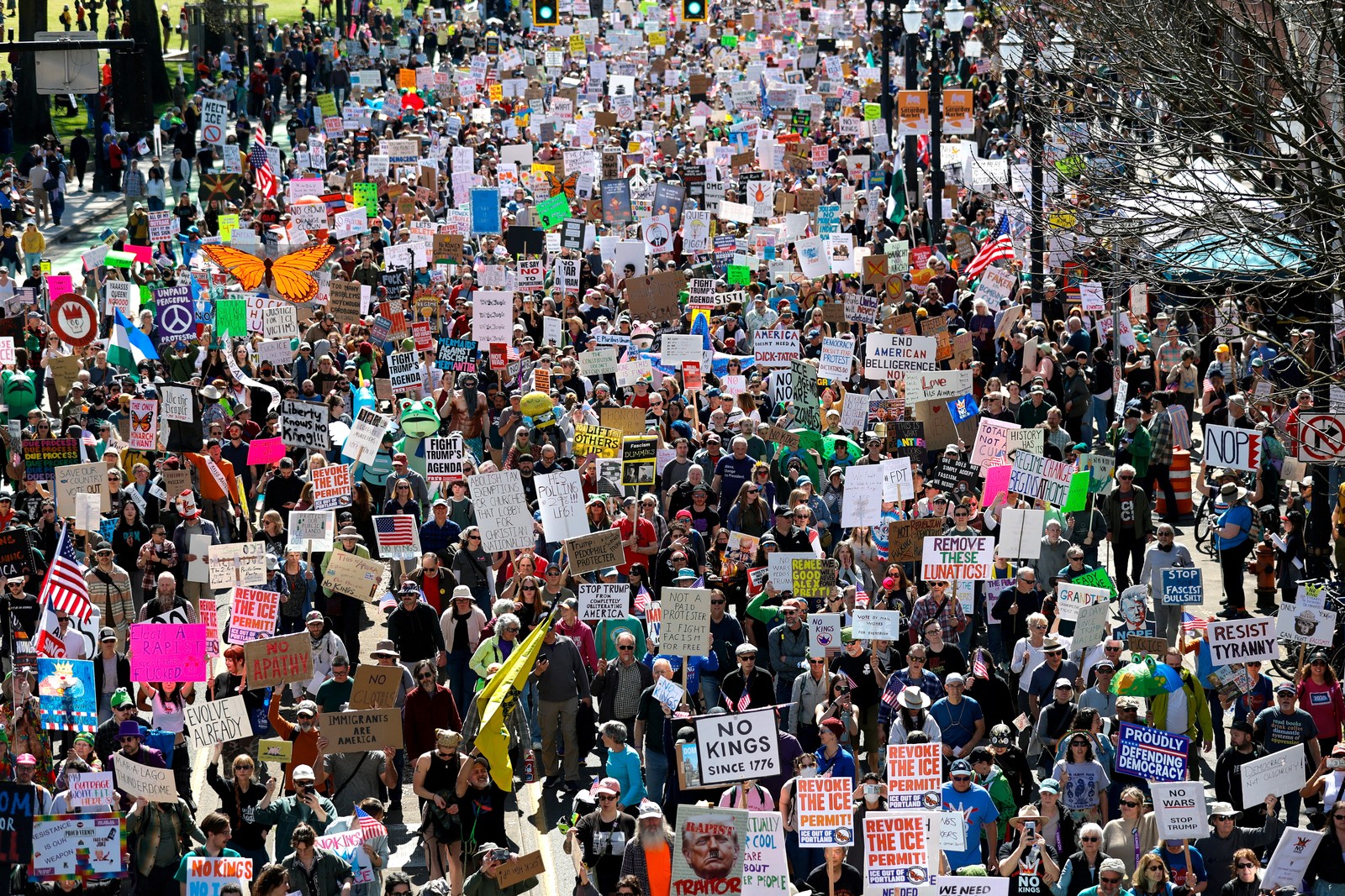 A large crowd of protesters marches down a street, carrying many anti-Trump signs.